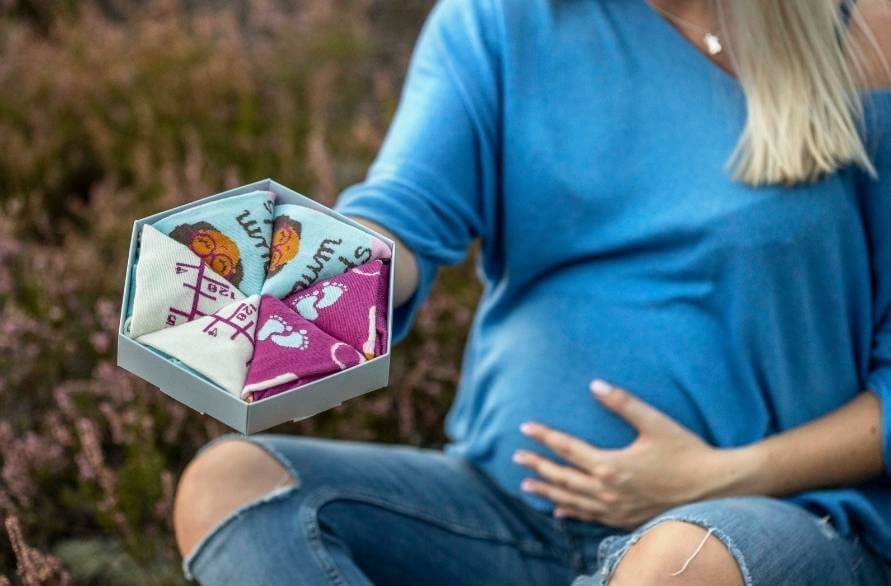 A pregnant woman holding a box of Rainbow Socks. 